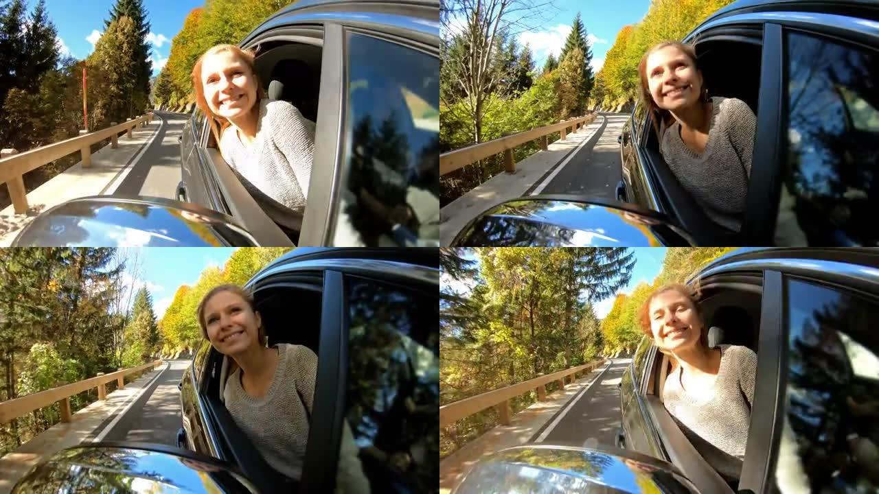 快乐的年轻女子在秋天的公路旅行中从车窗外倾斜