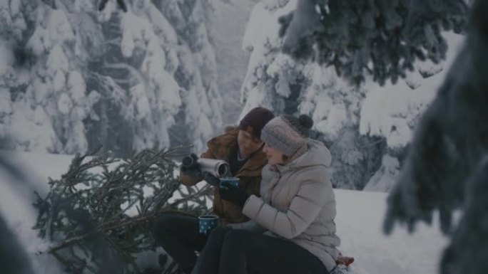 夫妇带着圣诞树在白雪覆盖的森林里享受热饮