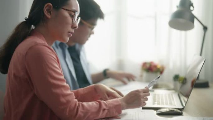 亚洲年轻夫妇使用计算器笔记本电脑在线用信用卡聊天做文书工作