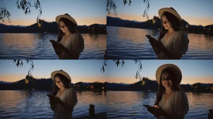 SLO MO年轻女子在黄昏时在布莱德湖使用她的智能手机