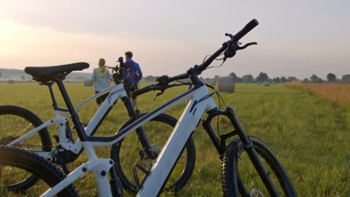 SLO MO夫妇骑自行车的人在日落时在草地上散步