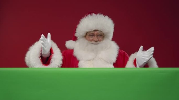 圣诞老人从他面前的绿色屏幕后面出现在红色背景的框架中
