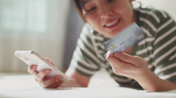 年轻的亚洲妇女用信用卡从手机上在线订购