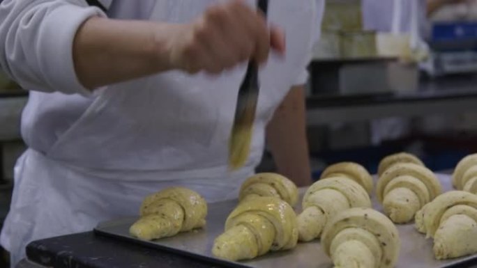 拉丁美洲面包师戴着口罩在工业面包店的羊角面包上撒上蛋黄