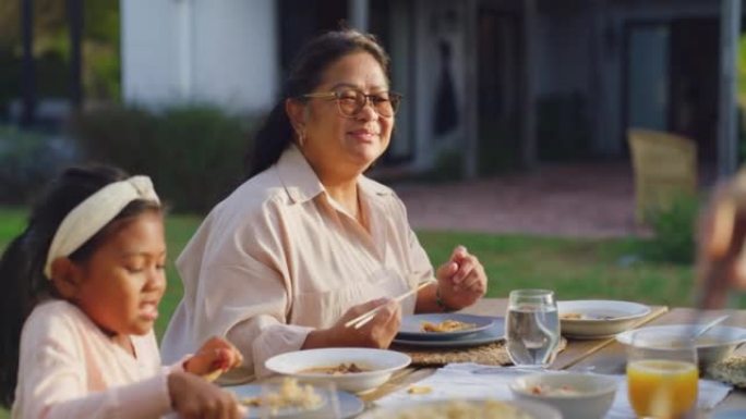 幸福的家庭在后院外面的桌子上一起吃饭。亚洲祖母和孩子坐在一起，在户外用餐区共进午餐或晚餐。玩得开心，