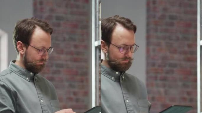 成功的小企业主使用平板电脑检查库存的垂直肖像。留着小胡子的英俊男人摆姿势拍照，在仓库储藏室里微笑着，