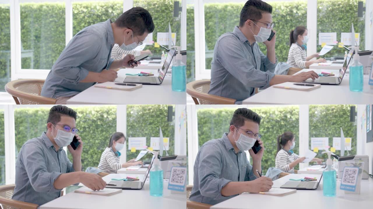 亚洲军官在办公室戴口罩与笔记本电脑一起工作。corona病毒危机后的社会距离衡量生活方式。在办公室一