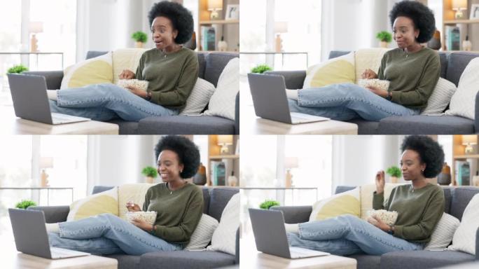 快乐的非洲裔美国妇女在笔记本电脑上播放在线电影，同时在爆米花上吃零食，在家里的沙发上放松。黑人女性在