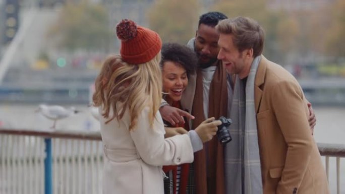 一群在户外穿着外套和围巾的朋友在伦敦秋冬之旅中看着相机上的照片-慢动作拍摄