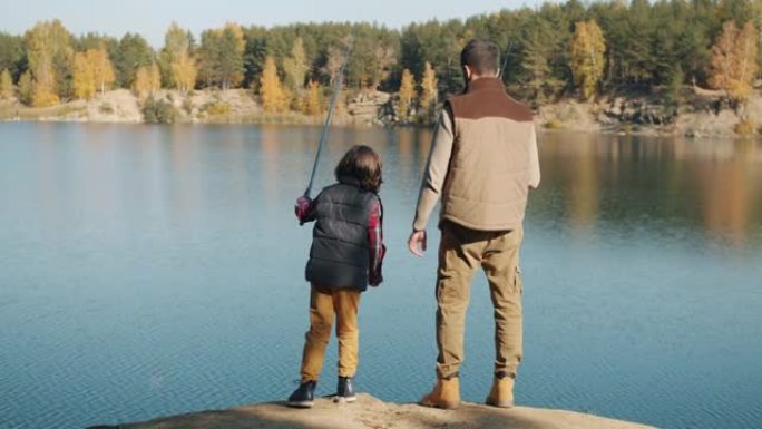 阳光明媚的秋天，成年男子和小男孩在湖里钓鱼的后景