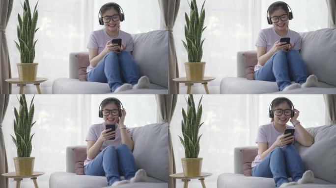年轻的亚洲女性在沙发上放松，在家里的客厅用耳机听音乐