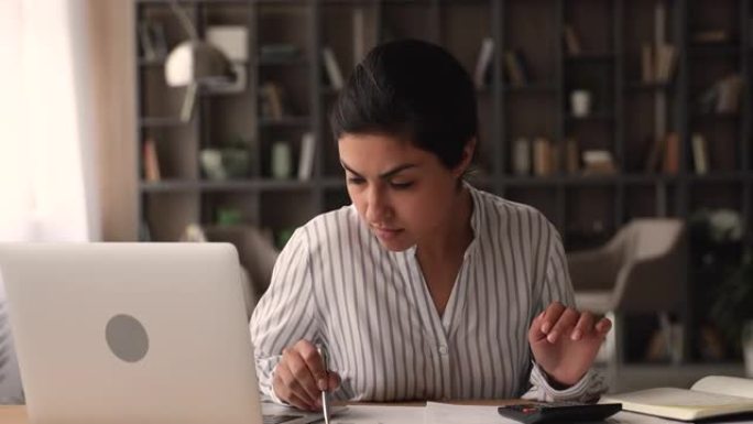 年轻的印度妇女坐在办公桌前使用计算器计算费用
