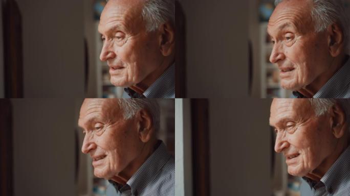 在阳光明媚的日子里，一个在家中的高级男子靠近窗户并透过窗户观看的肖像。一个微笑的老人看着他的孙子在院