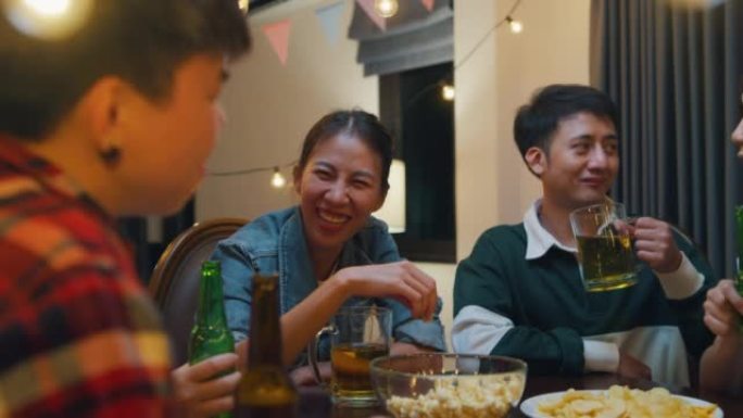 一群多民族的亚洲成人朋友喝酒精啤酒瓶玻璃和有趣的谈话笑声享受夜生活室内家庭餐桌上的聚会。