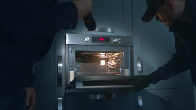 身穿制服的FBI探员在黑暗的厨房里拿着手电筒在烤箱里寻找物证