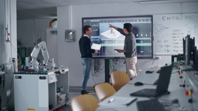 两名不同的男学生站在大屏幕附近，开发机械臂运动程序。教育和创新技术概念