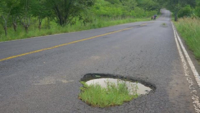 低角度: 草长在充满泥水的道路上的一个大洞周围。