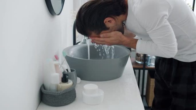 有魅力的家伙洗手和洗脸，然后抚摸着头发看着浴室里的镜子