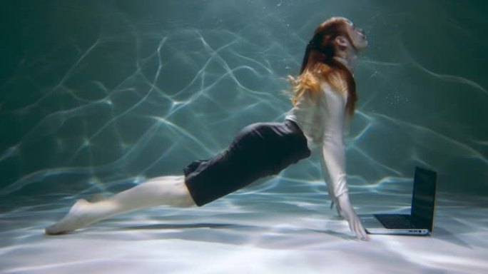 电影拍摄，年轻的红发女商人在水下使用笔记本电脑咨询客户，游泳慢动作。