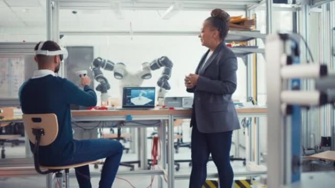 黑人高级工程师与戴着虚拟现实耳机的年轻男性计算机科学家交谈，他们使用控制器远程操纵机械手。高科技研究