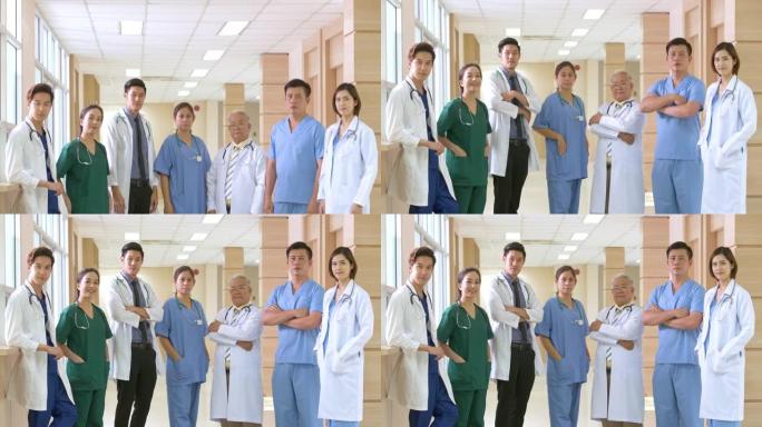 俯仰拍摄一群亚洲男女医生站着，微笑着看着医院走廊上的相机，双臂交叉。自信的医疗团队准备治疗他们的病人