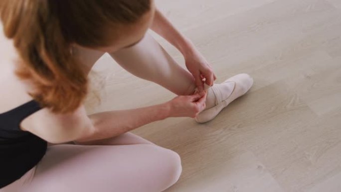 白人女芭蕾舞演员坐在工作室的地板上系芭蕾舞鞋