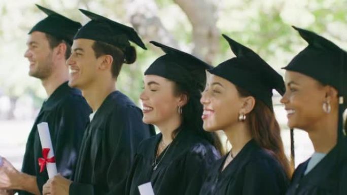 一群穿着砂浆板和长袍的大学或大学毕业生在外面的毕业典礼上排队。获得教育成功后持有学位或文凭的骄傲学生
