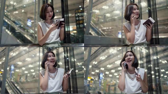 迷人的女人拿着智能手机和护照坐在透明电梯里