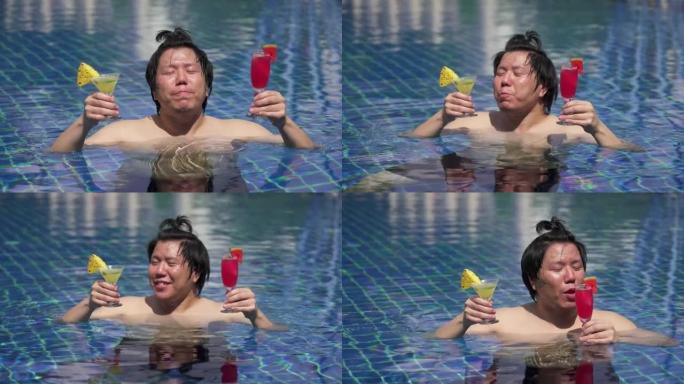亚洲青年快乐男子在游泳池里喝鸡尾酒。