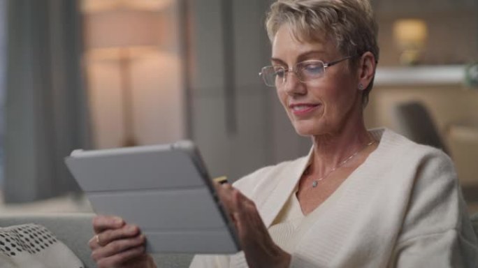 4k视频片段，一名高级妇女在数字平板电脑上浏览时拿着银行卡