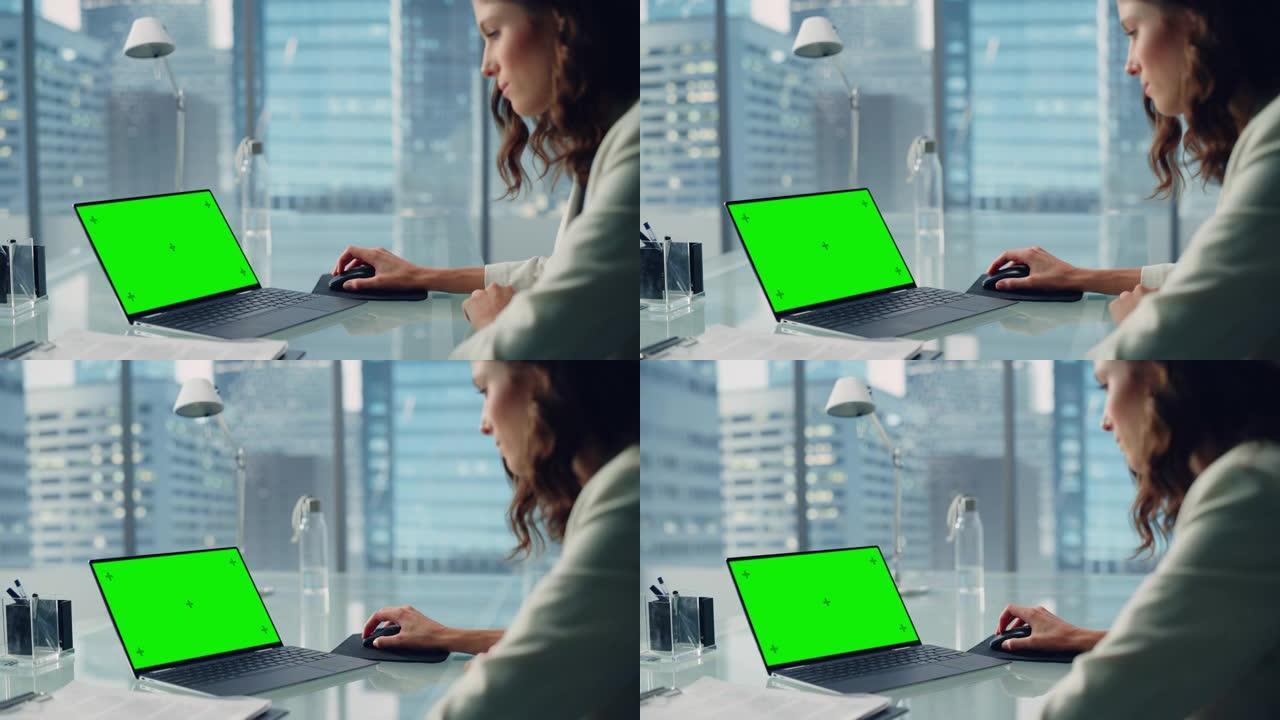 年轻成功的女商人坐在办公桌前，在城市办公室的绿屏色度钥匙笔记本电脑上工作。有才华的顶级经理为电子商务