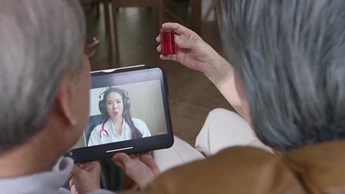 年迈的祖父和祖母拿着一瓶药咨询医生，用平板电脑作为视频通话，以缩小他们之间的距离，减少传播感染的机会