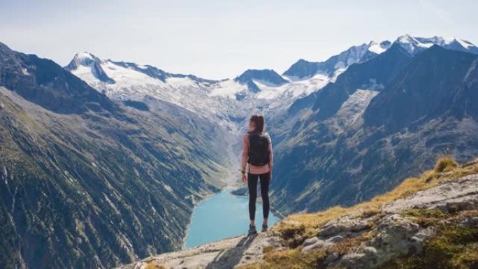 女徒步旅行者站在悬崖边，欣赏山谷湖和周围群山的壮丽景色