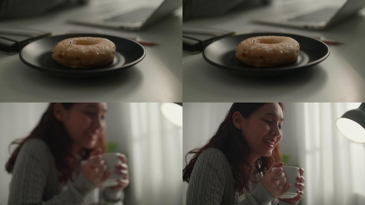年轻的亚洲妇女在家工作时吃甜甜圈
