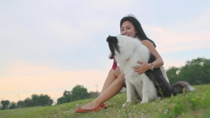 年轻的亚洲女孩和她的狗在自然公园享受美丽的夏日日落。