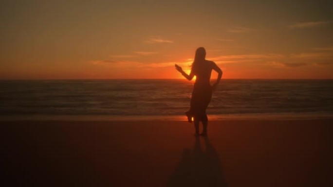 日落时在海滩上跳舞的年轻女子的SLO MO剪影
