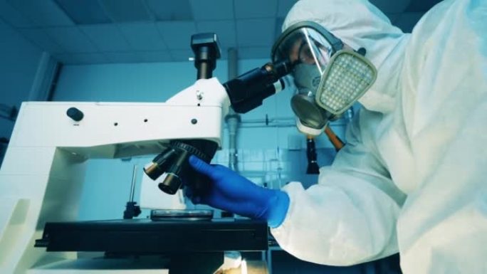一个穿着防护服的男人正在实验室操作显微镜