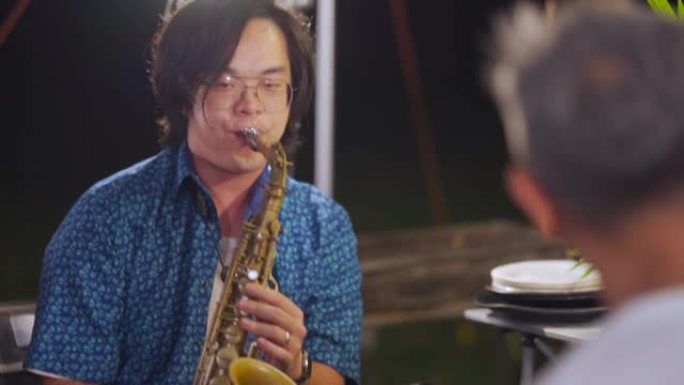 亚洲中国萨克斯风演奏家晚上在花园聚会露营帐篷中与家人和朋友一起演奏萨克斯风