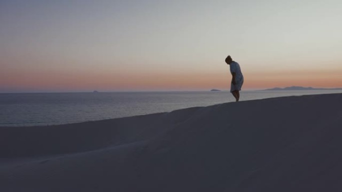 意大利撒丁岛日落时坐在海滩上的女人的景色。