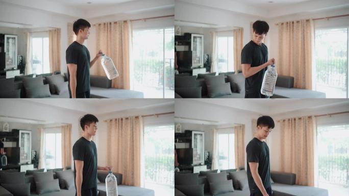 亚洲男子在家中使用塑料加仑水瓶代替健身房举重锻炼手臂二头肌