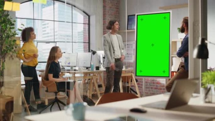 时尚的年轻项目经理在创意机构会议室的团队会议上讲话。同事在绿屏模拟色度键显示器上展示商业计划演示。