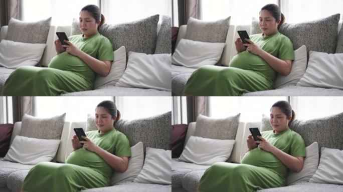 穿着绿色西装的孕妇在家中客厅沙发上使用手机