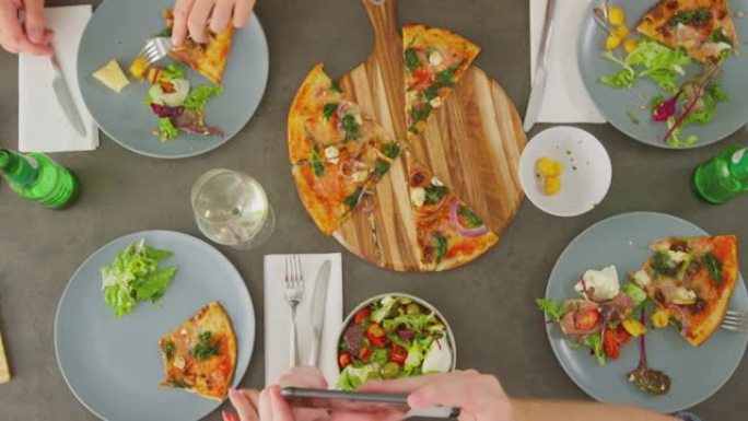 在意大利餐厅的朋友一起吃披萨并在手机上拍摄食物的俯视图-慢动作拍摄