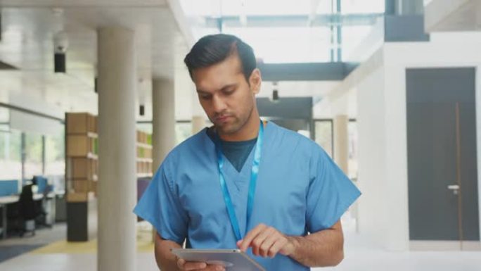 使用数字平板电脑在繁忙的医院大楼中穿行的磨砂膏中的男医生
