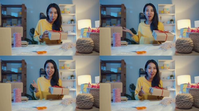 看着相机销售的快乐年轻亚洲女商人晚上在网上商店市场向客户视频直播介绍产品。