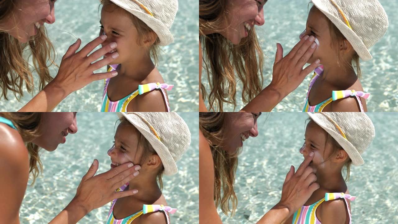 一个小女孩的肖像在海滩上笑着，而她的母亲在她的脸上涂了防晒霜。暑假期间，年轻女子保护女儿的皮肤免受阳
