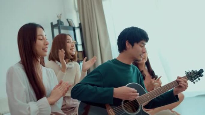 年轻的亚洲男子在一群年轻女子的包围下弹吉他，并在室内举行家庭聚会