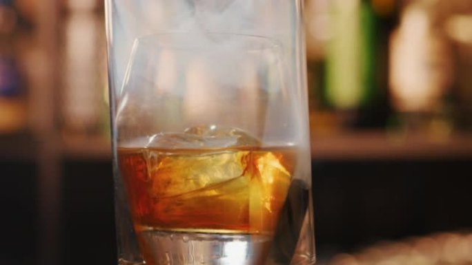 专业调酒师的特写镜头正在为酒吧或迪斯科俱乐部的顾客准备一杯带有冰块和烟雾的精英酒精鸡尾酒。