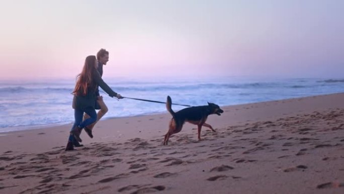 日落时，年轻夫妇在海滩上与狗一起奔跑