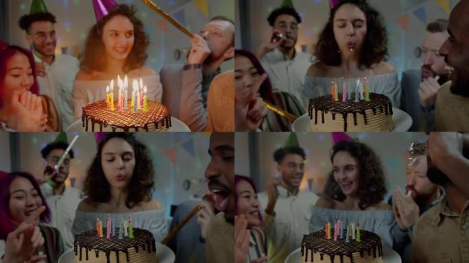 美味的生日蛋糕和戴着派对帽的年轻女子吹蜡烛的特写镜头与家里吵闹的朋友一起庆祝